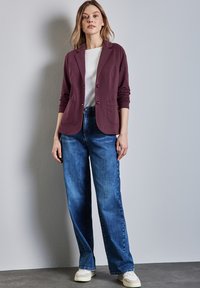 Paarse blazer met twee knopen en zakken over een wit shirt, gecombineerd met wijde blauwe denim jeans en witte sneakers.