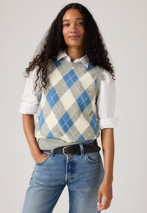 Argyle trui-vest in grijs, blauw en geel; heeft ruitpatronen en een geribde zoom. Gecombineerd met een wit overhemd met kraag en blauwe jeans.