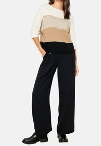 Lekki sweter w kolorowe bloki w kremowym, beżowym i czarnym kolorze; dzianinowy fason z łódkowym dekoltem. Połączony z czarnymi spodniami o szerokich nogawkach i butami.