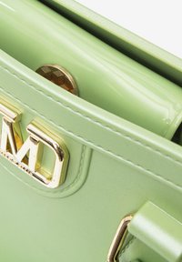 Groene glanzende handtas met gouden hardware, een gegraveerd logo en een gladde textuur. Interieur toont een hexagonaal muntvak.
