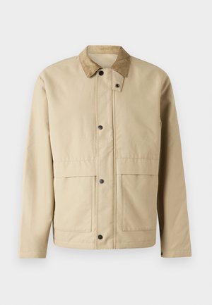 Beige bunda s korduroy límcem, patentkami, dvěma předními kapsami a mírně přiléhavým střihem. Vyrobena z hladkého materiálu.