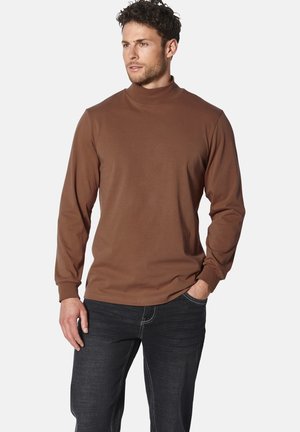 Brauner Langarm-Pullover mit Turtleneck aus glattem Stoff, mit figurbetonten Ärmeln und einer klaren Silhouette, kombiniert mit dunklen Jeans.