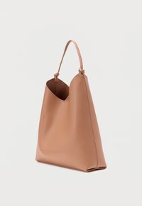 Καφέ δερμάτινη τσάντα tote με μινιμαλιστικό σχεδιασμό, που διαθέτει καμπυλωτό πάνω μέρος, μονό χερούλι και ομαλή υφή.