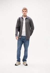 Grå skjorta över en vit t-shirt, tillsammans med blå jeans och beige sneakers. Modellen bär en svart väska.