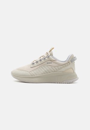 Baskets athlétiques beige clair avec dessus en mesh, perforations, accents gris et semelle texturée. Présente un logo sur le côté et des lacets.