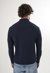Marineblauwe ribgebreide trui met een hoge kraag, lange mouwen en een aansluitend ontwerp, gecombineerd met lichtblauwe denim jeans.