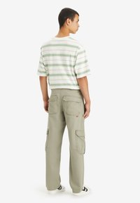 Majica s kratkimi rokavi v beli barvi z zelenimi črtami, v kombinaciji s svetlo kaki cargo hlačami, ki imajo več žepov in majhen logotip.