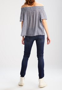 Top bez ramínek v námořnické modři a bílé kostkované, vyrobený z bavlny, s volánovými rukávy. Spárován s tmavými džíny a bílými kotníkovými botami.