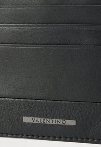 Juodas odinis kortelių dėklas su keliomis kortelių kišenėmis ir tekstūruota apdaila. Priekyje yra sidabrinė „Valentino“ plokštelė.