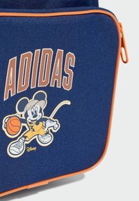 Torba od mornarsko plavog tkanog materijala s narančastim detaljima, na kojoj je crtani miš koji igra košarku te natpis "ADIDAS" ispisan podebljanim svijetlim slovima.