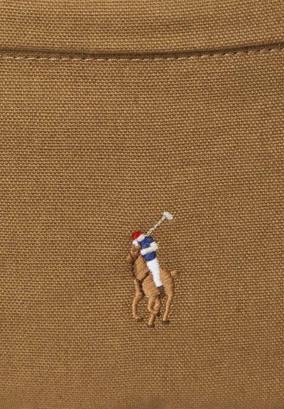 Geborduurd logo van een polo-speler in een blauw shirt en een rode helm op een bruine, gestructureerde stoffen achtergrond.