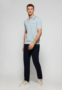 Polo de manga corta azul claro con detalles en negro, combinado con pantalones azul marino y zapatillas beige, con un corte ajustado y un logo sutil.