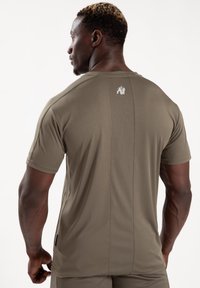 Olijfgroene sport T-shirt met korte mouwen, een aansluitende pasvorm en een klein grafisch logo op de bovenrug. Glad materiaal.