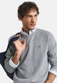 Grijze sweatshirt met een ronde halslijn en geribde boorden, gelaagd over een witte blouse met kraag, gecombineerd met een marineblauw schoudertas.