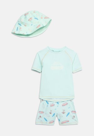 Šviesiai mėlynas kūdikio maudymosi kostiumėlis, susidedantis iš trumpomis rankovėmis marškinėlių, derančių šortų su banglentėmis ir „Vans“ motyvais, bei kibiro formos kepurės su panašiais raštais.