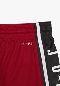 Pantalones cortos deportivos rojos y negros con cinturilla elástica, franja vertical blanca y "DRI-FIT" impreso en la tela roja.