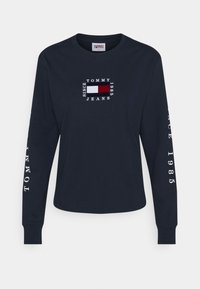 Laivastonsininen pitkähihaiste paita, jossa on valkoinen brodeerattu logo ja punainen suorakulmio. Varressa lukee "TOMMY JEANS" ja paita on pyöreäkaula-aukko.