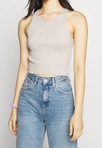 Jasnoszary prążkowany top na ramiączkach o dopasowanym kroju, zestawiony z jasnoniebieskimi spodenkami z wysokim stanem. Widoczne guziki i kieszenie na spodniach.