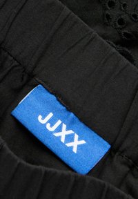 Μπλε ετικέτα ρούχου με λευκό κείμενο "JJXX" ραμμένη σε μαύρο υφασμάτινο ένδυμα.