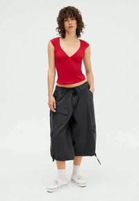 Punainen istuva yläosa, jossa syvä v-pääntie, yhdistettynä löysiin mustiin cargo-shortseihin. Shortseissa on taskut ja kiristysnauha vyötäröllä. Valkoiset tennarit täydentävät asun.