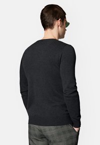 Ciemnoszary sweter z miękkiego materiału. Posiada okrągły dekolt i ściągacz u dołu. Model pokazany z tyłu, noszący okulary przeciwsłoneczne.