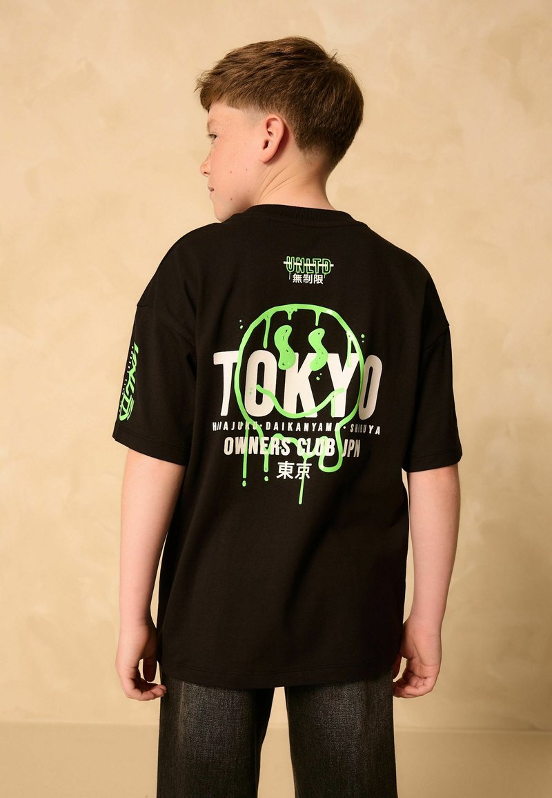 T-shirt nera oversize in cotone con testo e grafiche in stile graffiti verdi "TOKYO" sul retro, maniche corte e vestibilità rilassata.