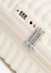 Walizka z twardą skorupą w kremowym kolorze z żebrowaną fakturą. Wyposażona w zamek TSA, pokrętło do ustawiania kombinacji oraz srebrne suwaki z nazwą marki.