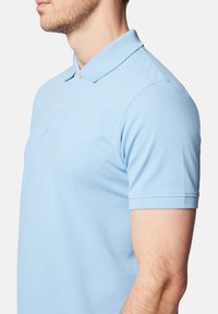 Jasnoniebieska koszulka polo wykonana z bawełny. Posiada klasyczny kołnierzyk, krótkie rękawy oraz dwa guziki z przodu. Gładki, teksturowany materiał.