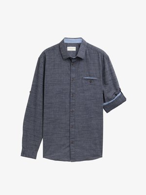 Temno modra, teksturirana majica z dolgimi rokavi, spredaj z gumbi in žepom na prsih; ovratnik je obdan s svetlejšo modro poudarjenostjo. Možnost zavihanih rokavov.