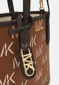 Brun læder tote taske med gentagende MK logo, mørkebrune håndtag og guld MK charm samt Michael Kors navneskilt.
