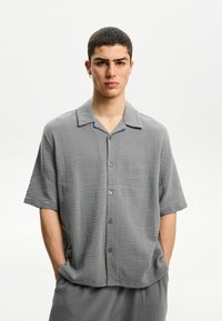 Short-sleeve, collared shirt in textured gray fabric with a relaxed fit. Features a button front and subtle horizontal pattern.