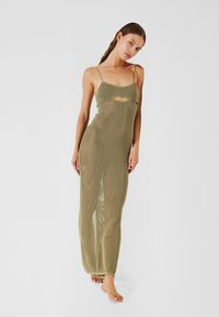 Vestido maxi de punto en verde oliva con tirantes finos, que presenta un corte central y una textura de tejido abierto en toda la prenda.