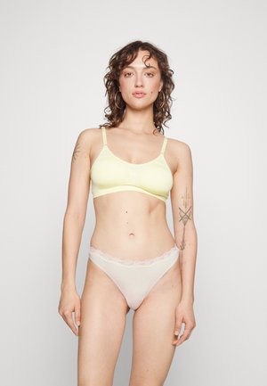 Soutien-gorge sans fil jaune clair avec des bretelles ajustables, associé à un string nude transparent avec une bordure en dentelle. Tissu lisse et extensible.