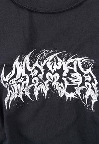 Μαύρο βαμβακερό t-shirt με μεγάλο λευκό γραφικό κείμενο με αιχμηρά, γωνιώδη γράμματα. Λείο ύφασμα, στρογγυλή λαιμόκοψη, κοντά μανίκια.