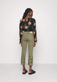 Camisa preta de manga longa com padrão floral e abertura nas costas, combinada com calças curtas verdes-oliva com bordados florais e sapatos pretos de deslizar.