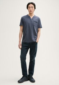 Navy pruhovaná krátká rukávová henley košile s náprsní kapsou, zkombinovaná s tmavě modrými džíny a černými teniskami. Čistý, neformální design.