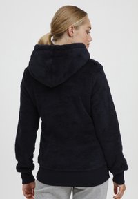 Navy blue hoodie made of soft, plush fabric with a large hood, ribbed cuffs, and hem. Displays a textured, cozy appearance.