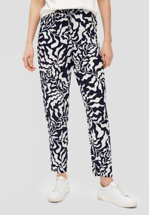 Pantalons bleu marine et blancs à motif de feuilles avec une taille élastique, coupe slim et longueur cheville, associés à des baskets blanches.