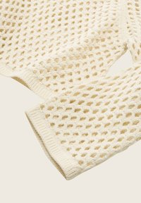Pull en mailles ouvertes de couleur crème. Présente un design texturé avec un motif en nid d'abeille et des poignets côtelés. Matière douce et respirante.