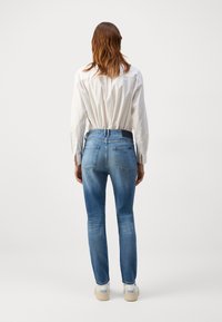 Niebieskie dżinsy o slim fit, średnim stanie i pięciu kieszeniach. W zestawieniu z białą koszulą z guzikami, noszoną na wierzchu.