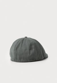 Casquette plate grise avec des panneaux cousus et un petit bouton sur le dessus, présentée sur un fond blanc.