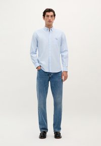 Lichtblauwe overhemd met lange mouwen en knoopsluiting, voorzien van een borstzak, met subtiele borduursels, gecombineerd met vervagende blauwe rechte jeans en zwarte schoenen.