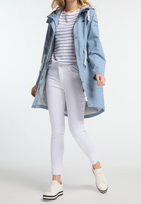 Femme portant une veste à capuche bleu clair, un t-shirt à rayures blanches, un jean skinny blanc et des baskets blanches à plateforme, marchant vers l'avant.