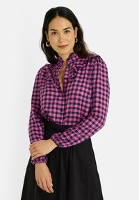 Camisa de cuadros rosa y azul marino con cuello y puños con volantes. Fabricada en tejido ligero, cuenta con cierre de botones y mangas largas.