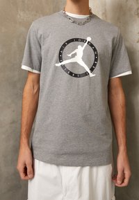 Persona que lleva una camiseta gris de Air Jordan Flight Club con una silueta blanca de un jugador de baloncesto, combinada con pantalones cortos blancos.