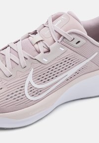 Světle růžová sportovní obuv s síťovaným svrškem, dekorativním prošíváním, bílým logem swoosh a polstrovanou podrážkou označenou jako "ComfiRide."