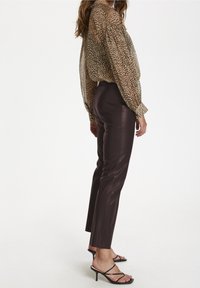 Transparent leopardmönstrad blus med långa ärmar. Kombinerad med åtsittande, mörkbruna, syntetiska läderbyxor och svarta högklackade sandaler med remmar.