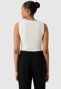 Top blanco sin mangas con textura acanalada, combinado con pantalones negros que tienen bolsillos frontales. El diseño es ajustado y minimalista.