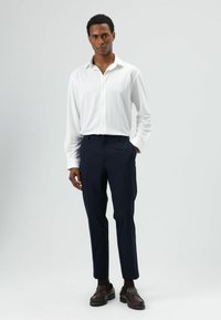 Weißes Langarmhemd, marineblaue Hose und dunkelbraune Loafers. Schlanke Passform und glatte Textur. Minimalistisches Design ohne Muster.