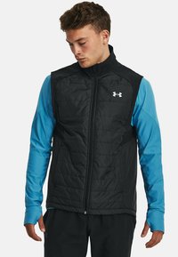 Gilet noir isolé avec un col montant, fermeture éclair et poches latérales. Présente un logo distinct de Under Armour sur la poitrine.